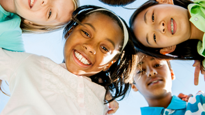 4 children with big smiles and their arms around each other standing in a circle, looking down into the camera