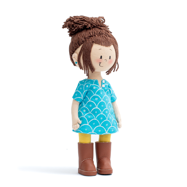 Mini Ava Handmade Cultural Doll in her blue long shirt, yellow pants and brown boots showing the doll from her right profile 