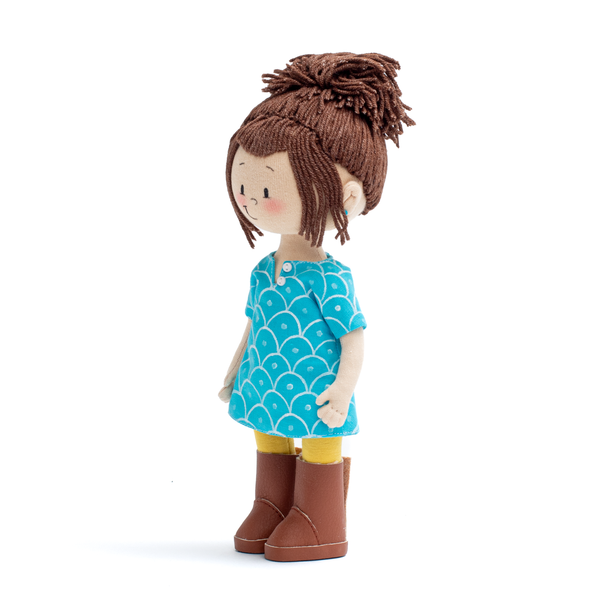 Mini Ava Handmade Cultural Doll in her blue long shirt, yellow pants and brown boots showing the doll from her left profile 