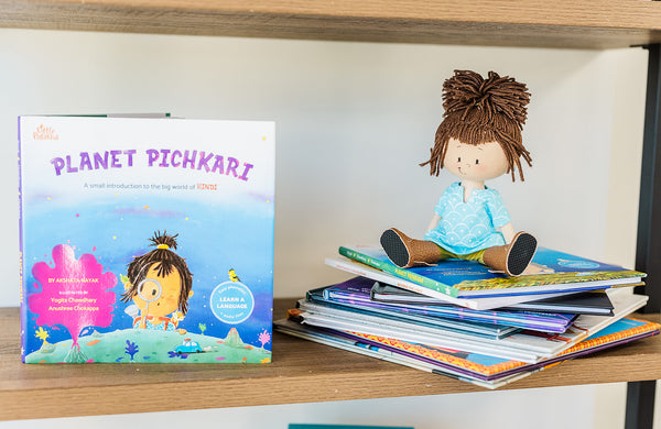 Little Patakha products Planet Pichkari Hindi Language Learning Book and Mini Ava Cultural Doll sitting on top of a pile of books on a shelf